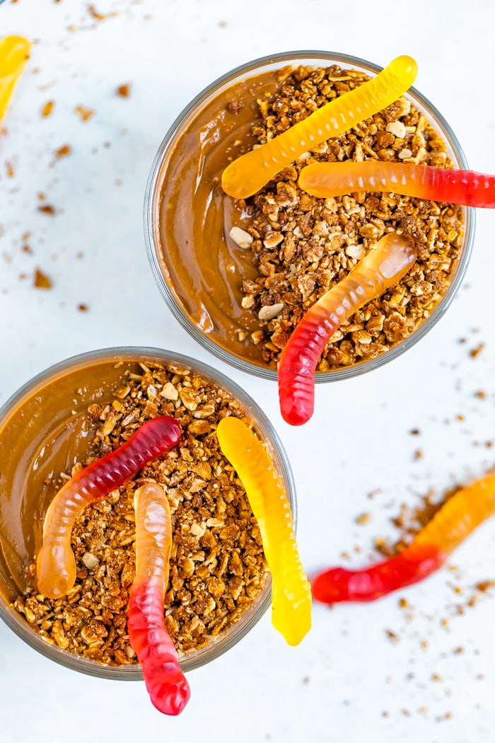 Two dirt pudding cups topped with granola and gummy worms.