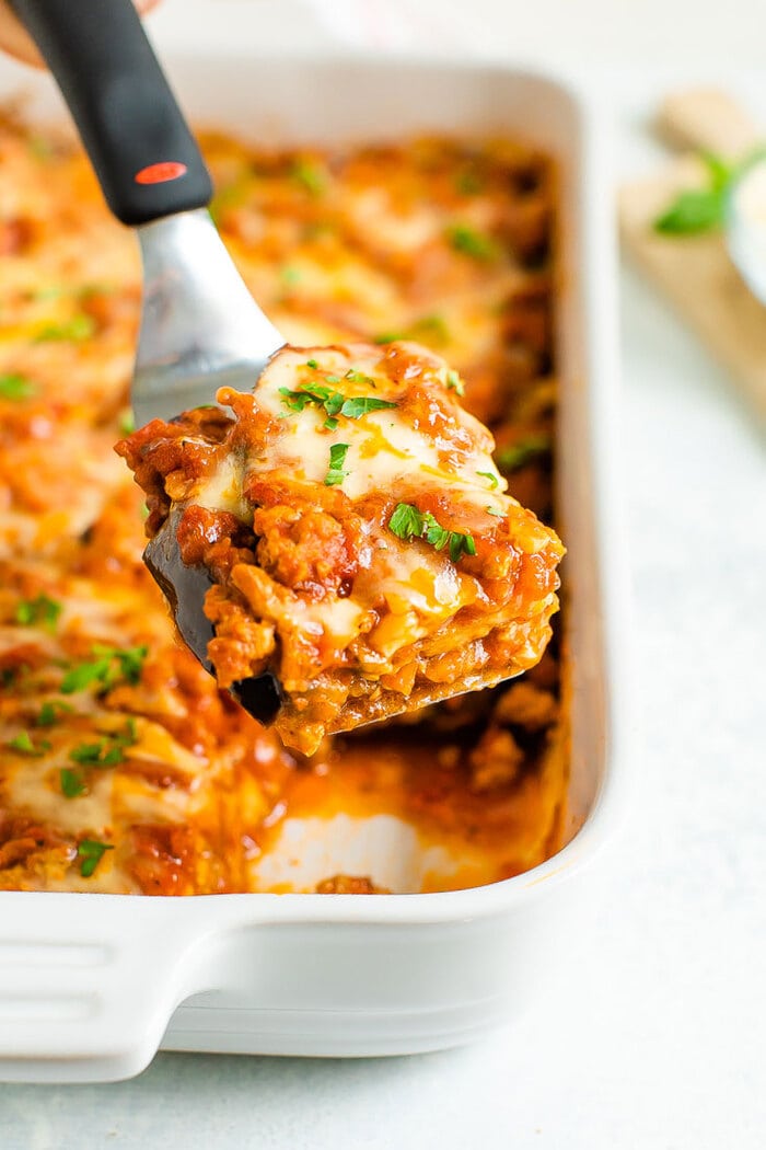 Spatula lifting a slice of cheesy eggplant casserole out of the casserole dish.