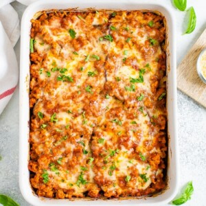 Baking dish of a cheesy eggplant casserole topped with cheese and fresh parsley.