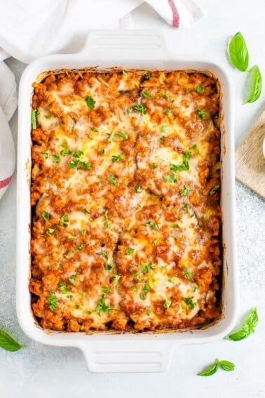 Baking dish of a cheesy eggplant casserole topped with cheese and fresh parsley.