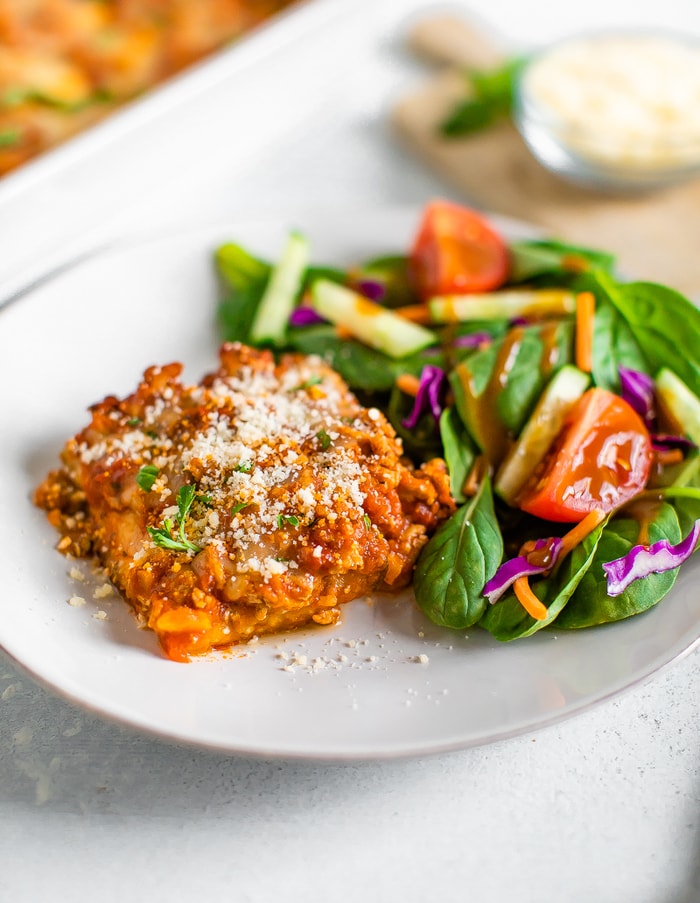 Serving of cheesy eggplant turkey casserole on a plate with a green salad.