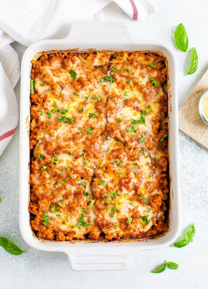 Baking dish of a cheesy eggplant casserole topped with cheese and fresh parsley.