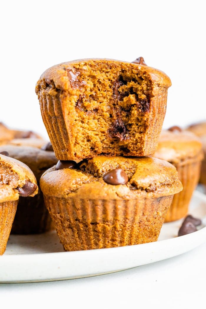 Two healthy pumpkin muffins stacked with a bite taken out of the top muffin.