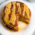 Stack of pumpkin pancakes, drizzled with peanut butter and maple syrup, with a bite taken out of the stack.