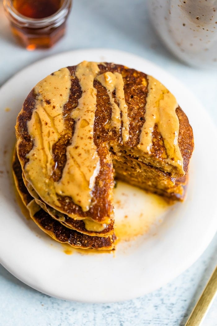 Stack of pumpkin pancakes, drizzled with peanut butter and maple syrup, with a bite taken out of the stack.