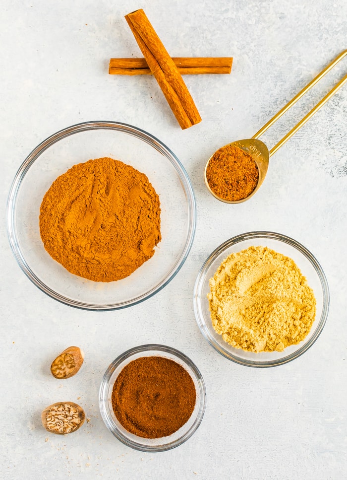 Spices in small glass bowls, a measuring spoon, and two sticks of cinnamon.