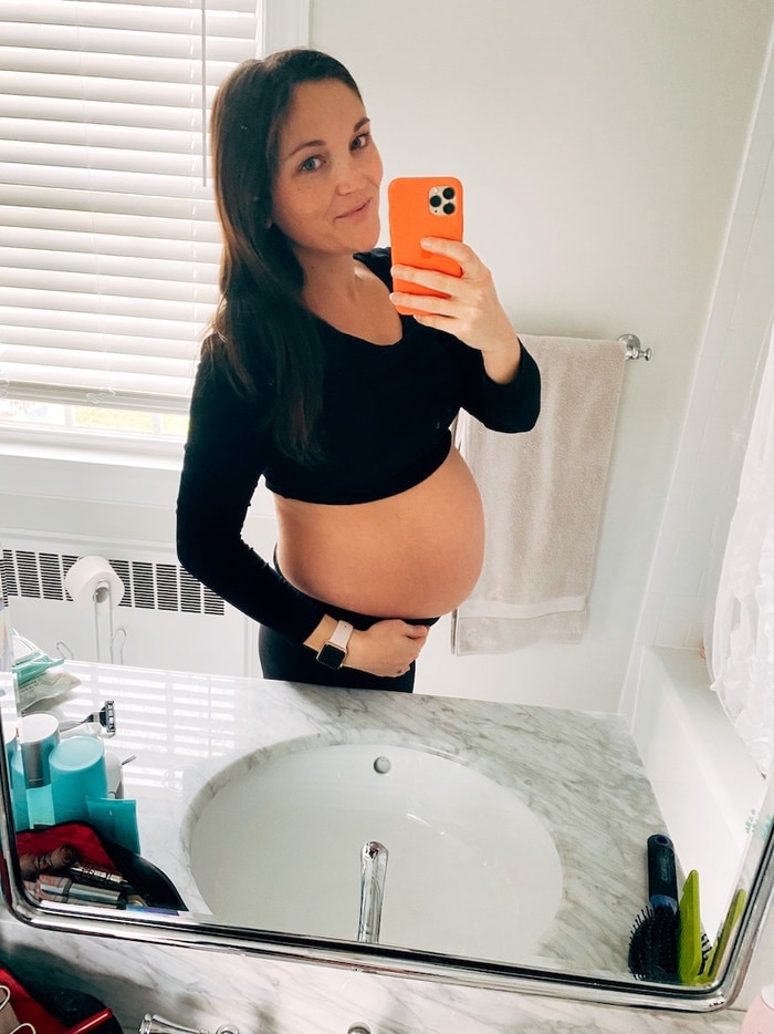 Woman in all black taking a mirror selfie at 40 weeks pregnant.