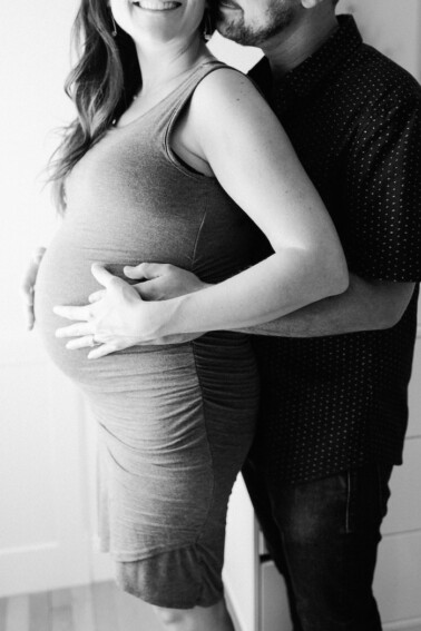 Heterosexual couple embracing for a maternity portrait in black and white.