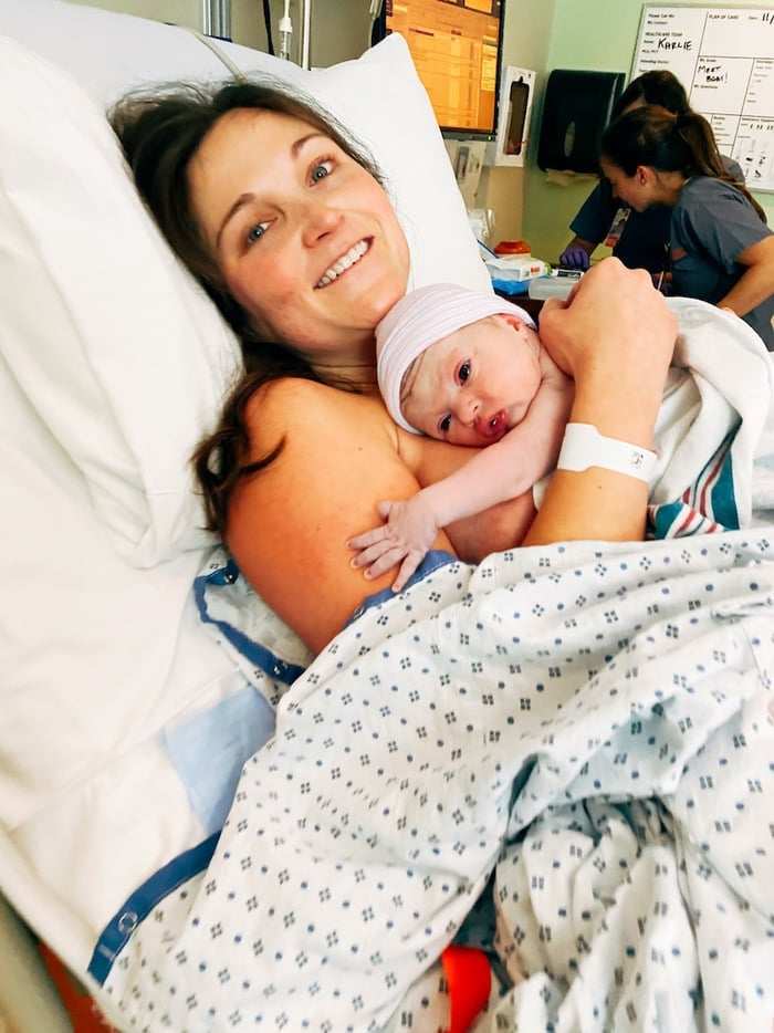 Mother smiling and holding her newborn baby in the hospital bed.