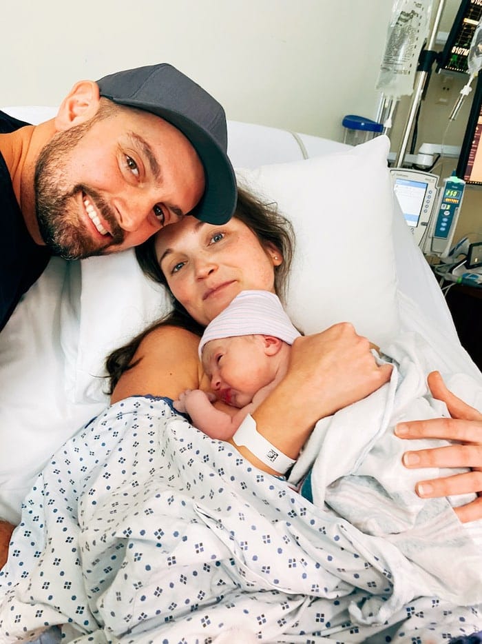 Couple smiling and holding their newborn baby girl in the hospital.