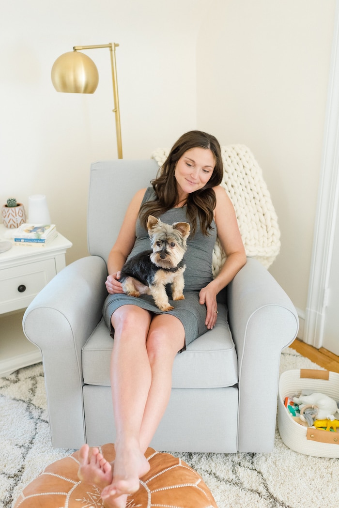 Pregnant woman sitting in glider with dog on lap.