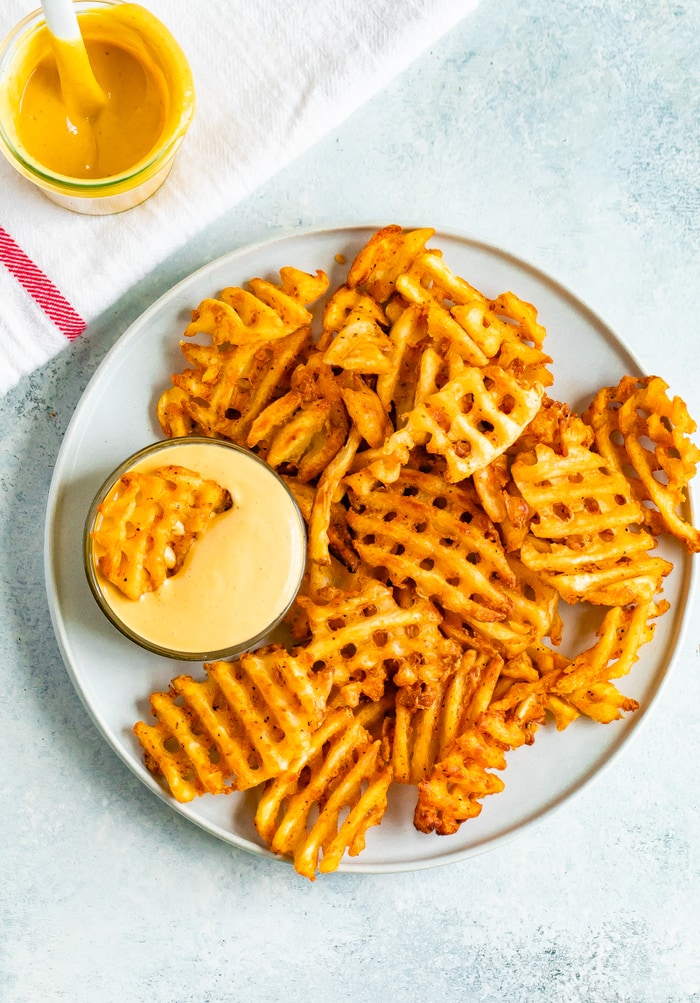 Plate of waffle fries with a bowl of Chick-Fil-A Sauce that one fry is being dipped into.