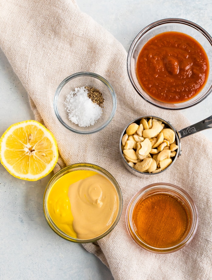 Ingredients to make homemade healthy Chick-Fil-A Sauce in bowls: bbq sauce, salt and pepper, cashews, lemon, mustard, and honey.