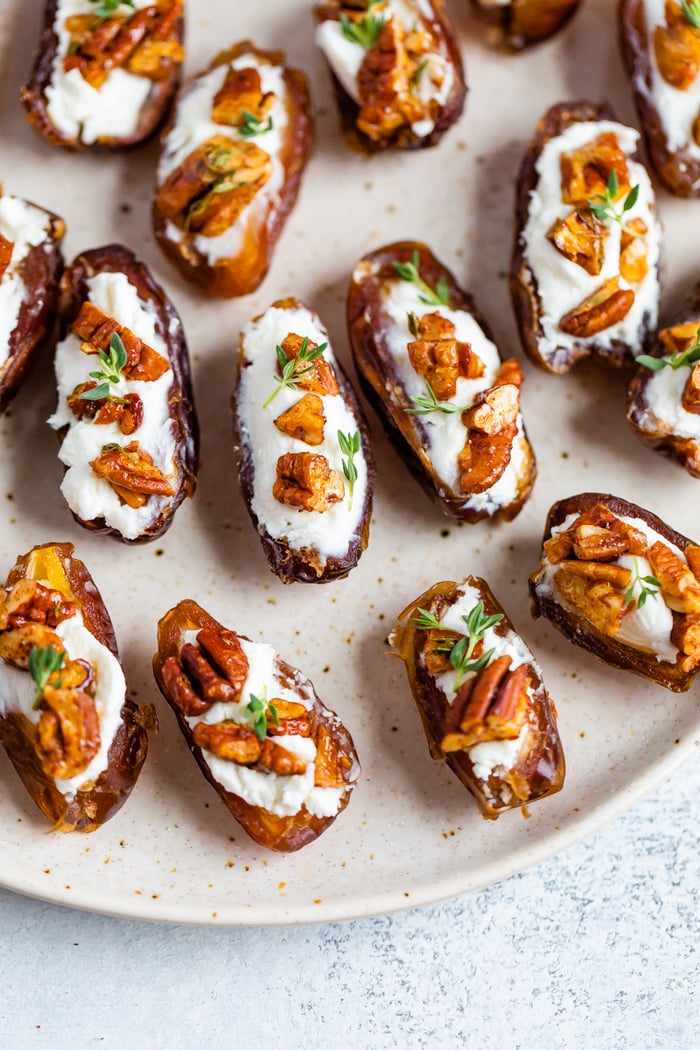 Close up photo of stuffed dates on a plate. The dates are stuffed with goat cheese, roasted pecans, and fresh thyme.