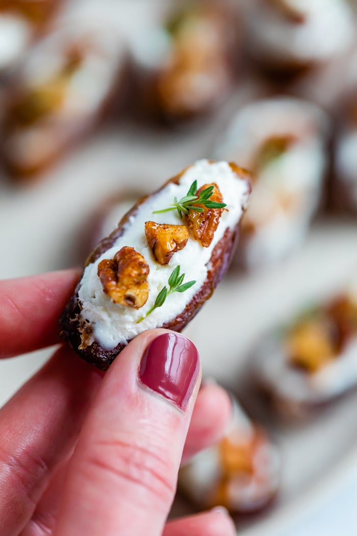 Hand holding a goat cheese stuffed date, topped with chopped pecans and fresh thyme.