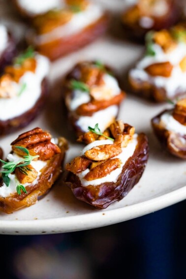 Close up photo of stuffed dates on a plate. The dates are stuffed with goat cheese, roasted pecans, and fresh thyme.