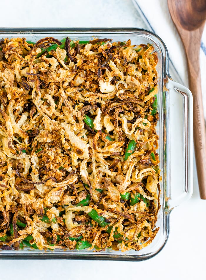 Casserole dish with healthy green bean casserole topped with crispy onions. A wood spoon is beside the baking dish.