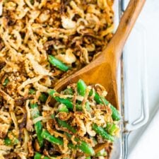 A wooden spoon scooping green bean casserole out of a glass baking dish.