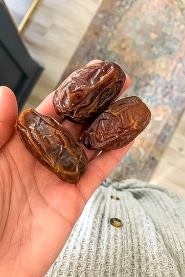 Three medjool dates in a palm of a women's hand.