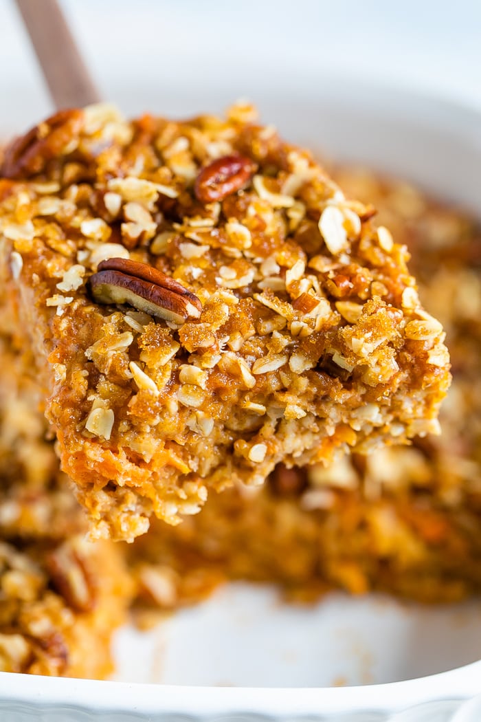 Wood spoon with a serving of baked sweet potato oatmeal topped with pecans.