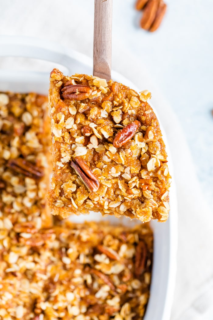 Wood spoon with a serving of baked sweet potato oatmeal topped with pecans.