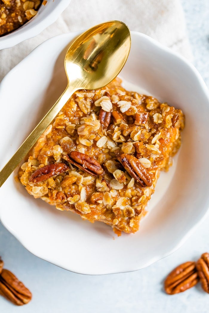 Plate with a serving of sweet potato baked oatmeal topped with pecans. A gold spoon is resting on the side of the plate.