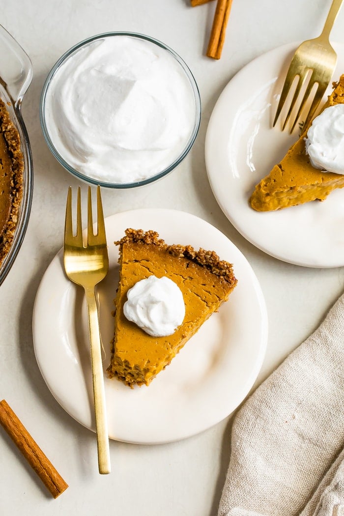 Tables with plates of slices of vegan pumpkin pie. Forks and a bowl of whipped cream are to the side.
