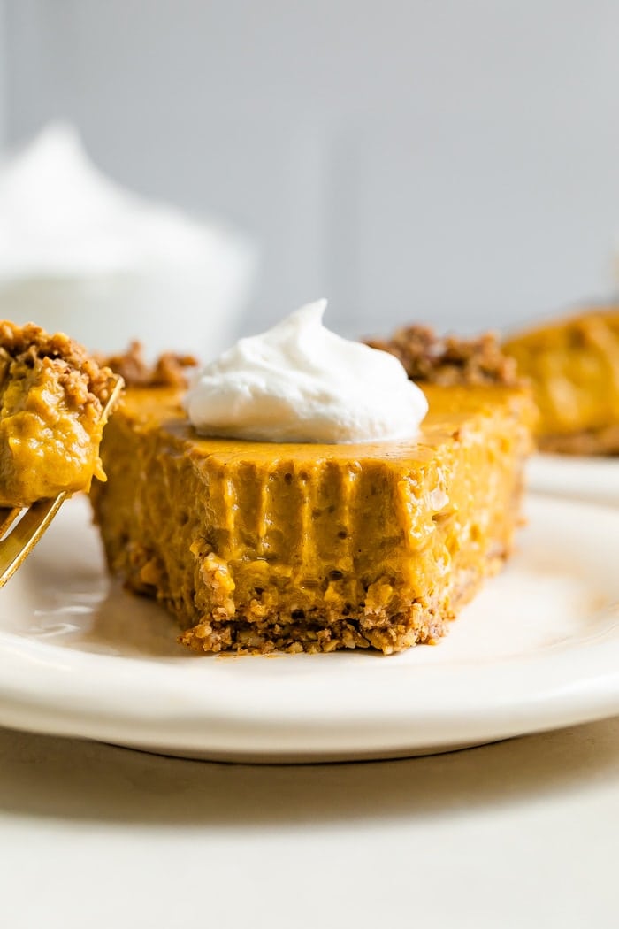 Slice of vegan pumpkin pie on a plate with whipped cream on top.