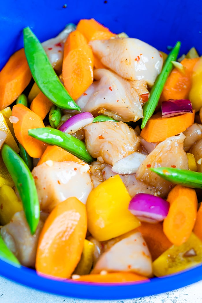 Mixing bowl with asian marinade, chicken, carrots, onions, peppers, and snap peas.