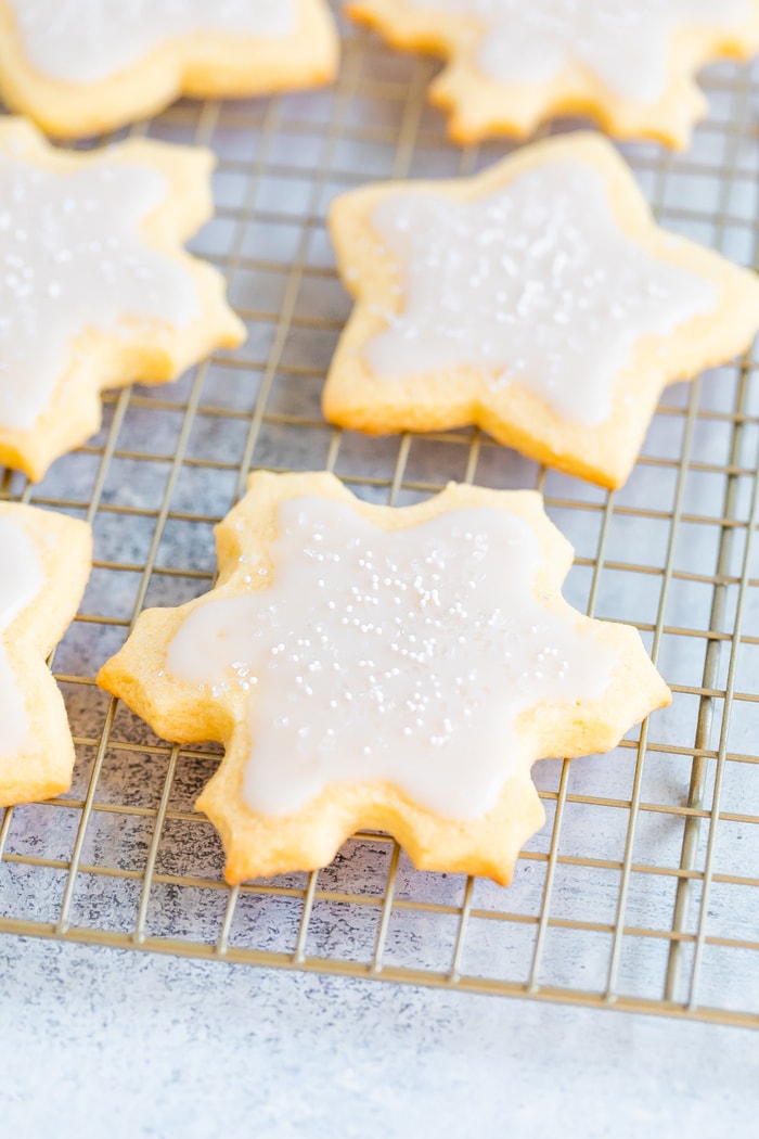 Snowflake and star cut-out cookies on a cooling rack decorated with white icing and sprinkles.