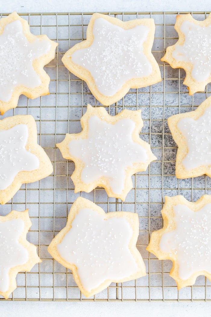 Snowflake and star cut-out cookies on a cooling rack decorated with white icing and sprinkles.