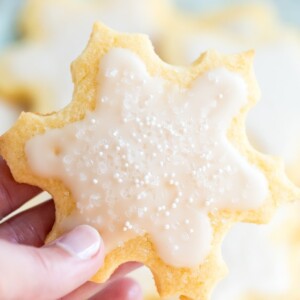 Hand holding a snowflake cut out cookies decorated with white icing and sprinkles.