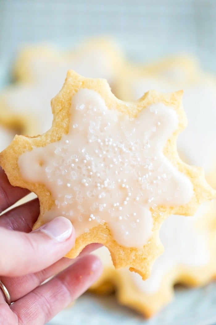 Hand holding a snowflake cut out cookies decorated with white icing and sprinkles.