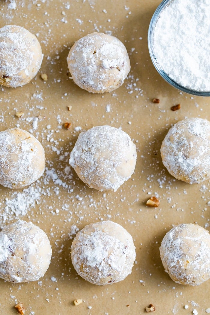 Snowball cookies on parchment paper next to a bowl of powdered sugar.