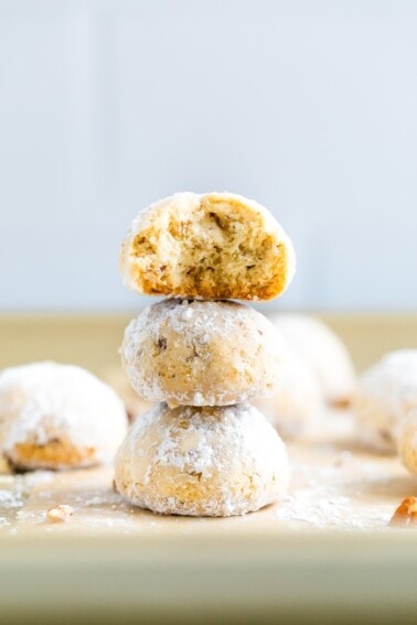 Stack of three snowball cookies on parchment paper. The top one has a bite taken out of it.