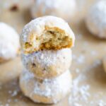 Stack of three snowball cookies on parchment paper. The top one has a bite taken out of it.