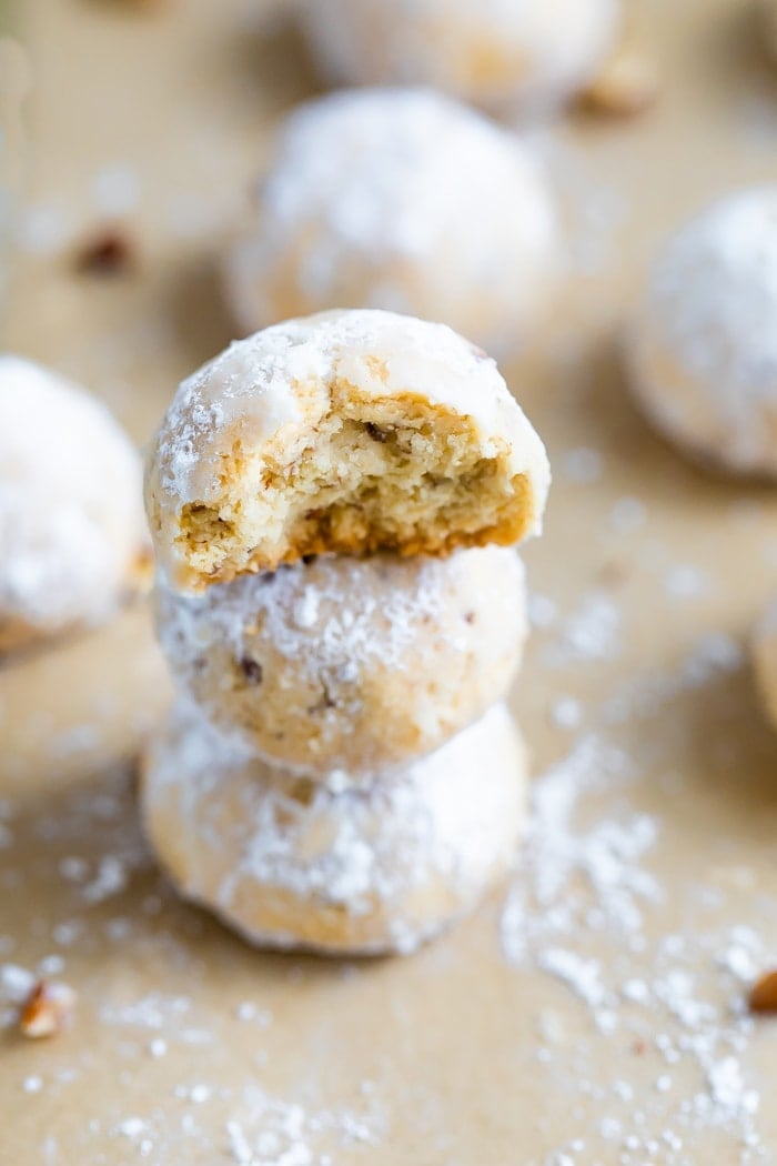 Stack of three snowball cookies on parchment paper. The top one has a bite taken out of it.