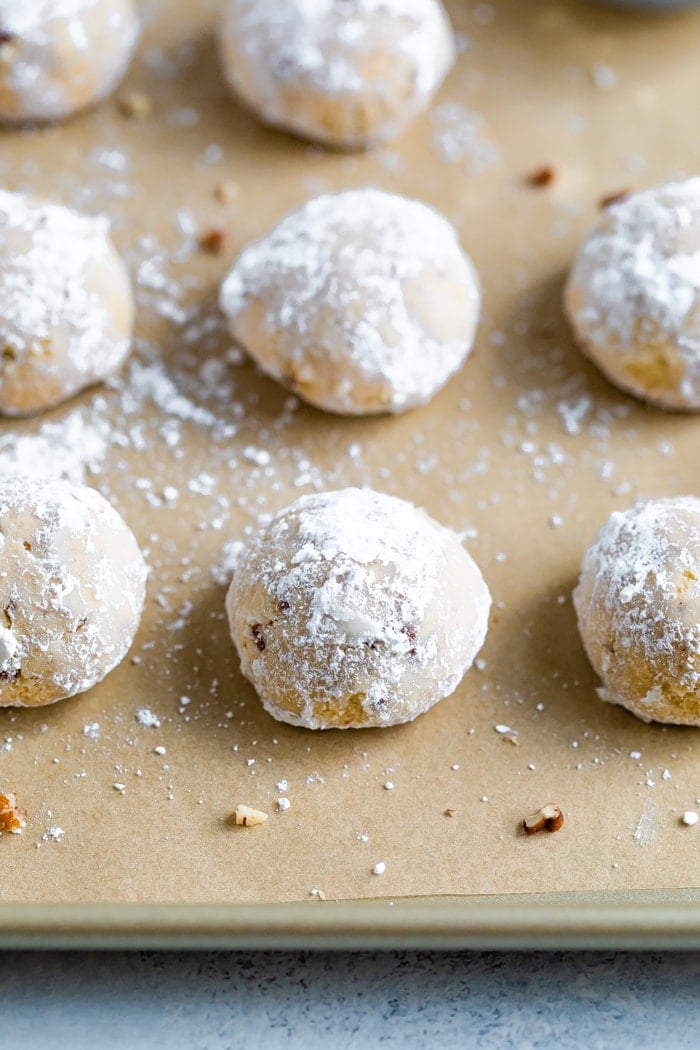 Snowball cooking on parchment paper surrounded by chopped pecans and powdered sugar.