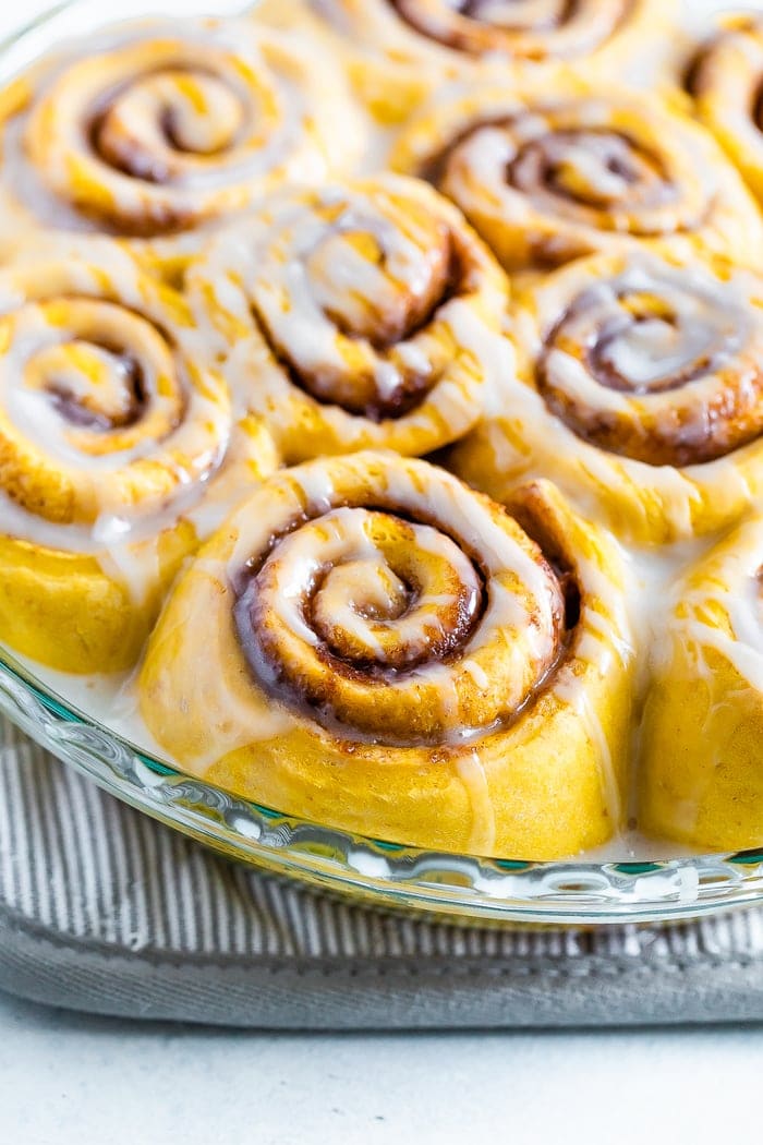 Round baking dish with pumpkin cinnamon rolls drizzled with icing.