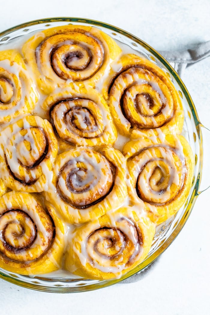 Round baking dish with pumpkin cinnamon rolls drizzled with icing.