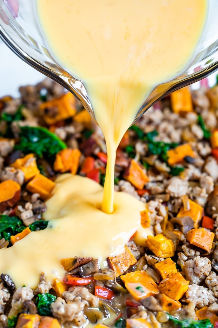 Egg mixture being poured over chicken sausage and veggies in a casserole dish.