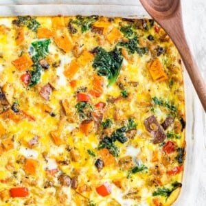 Casserole dish with an egg, veggie, and chicken sausage bake. A wood serving spoon is to the side.