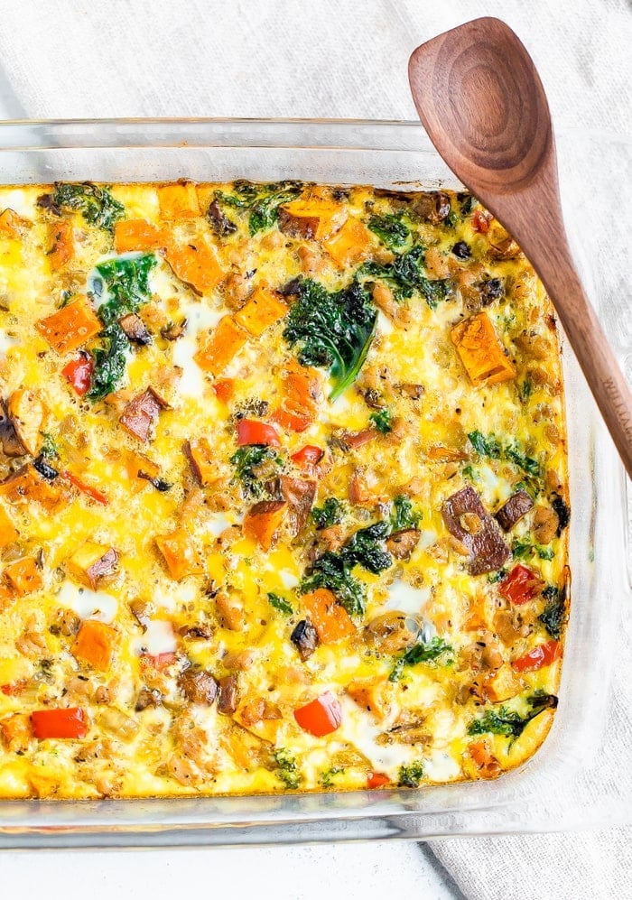 Casserole dish with an egg, veggie, and chicken sausage bake. A wood serving spoon is to the side.