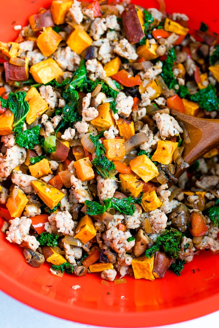 Mixing bowl with cooked ground chicken sausage, kale, sweet potatoes, peppers, and onions mixed with a wood spoon.