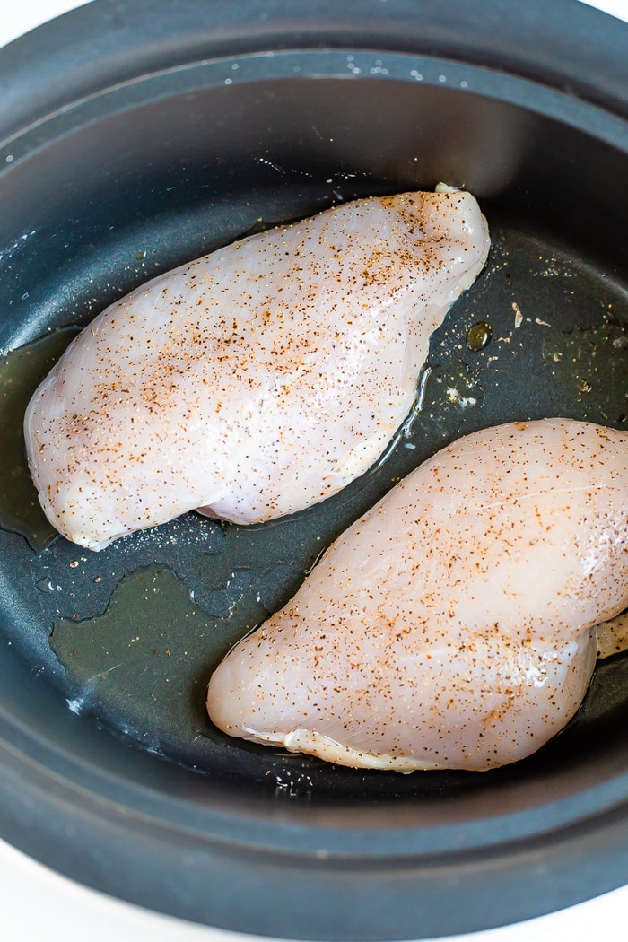 Two chicken breasts in a slow cooker with salt, pepper, and olive oil.