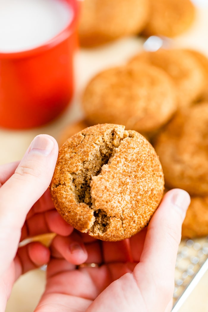 Hand breaking in half a snickerdoodle cookie. A mug of milk is in the background.