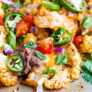 Close up of cauliflower nachos baked on a sheet pan and topped with beans, cheese, onions, peppers and cilantro.