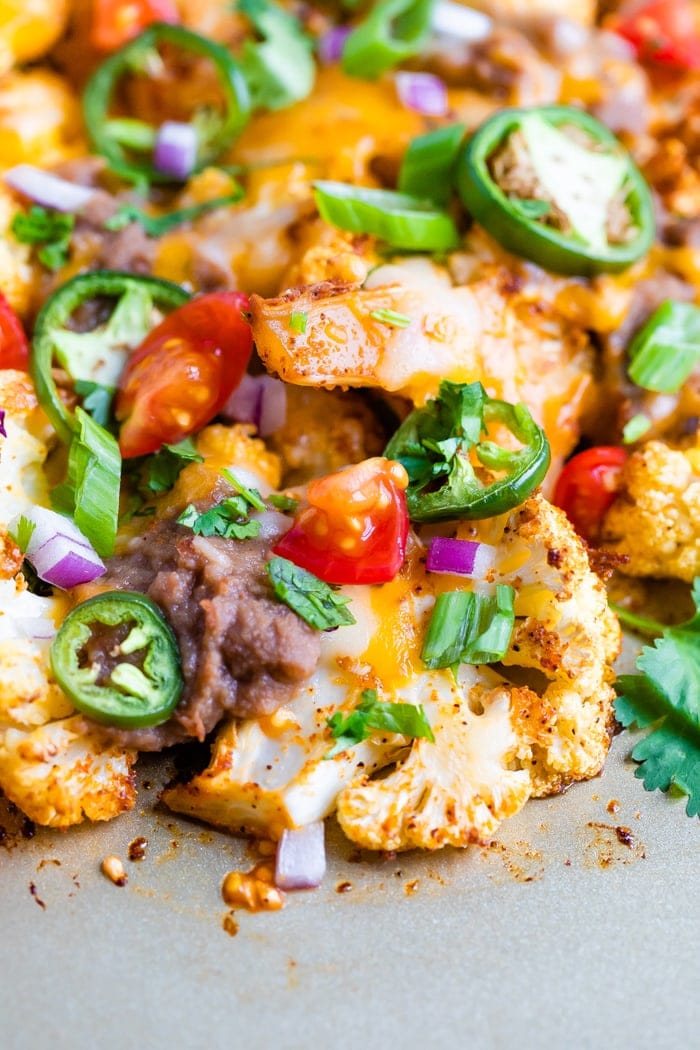 Close up photo of spiced cauliflower nachos baked with beans, cheese and veggies.