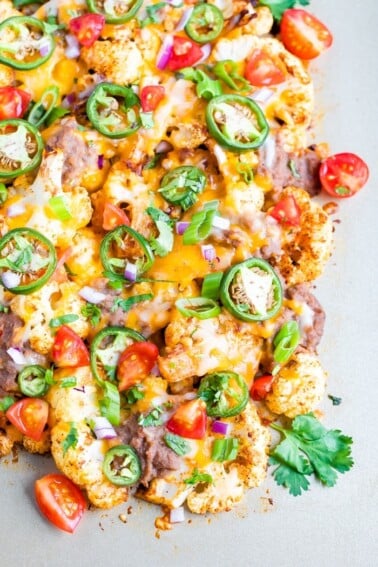 Cauliflower nachos baked on a sheet pan and topped with beans, cheese, onions, peppers and cilantro.