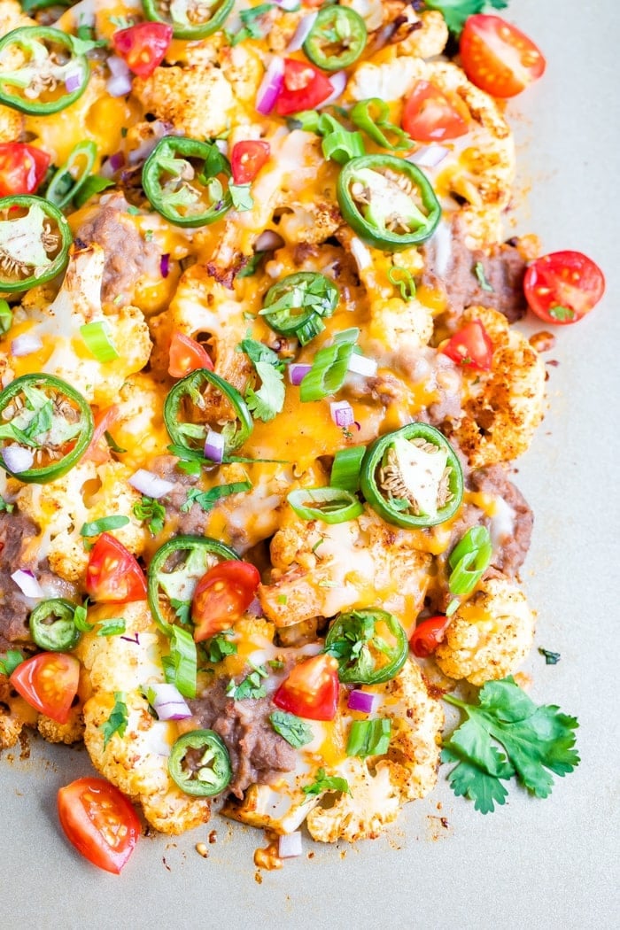 Cheesy baked cauliflower nachos on a sheet pan and topped with onion, peppers and tomato.